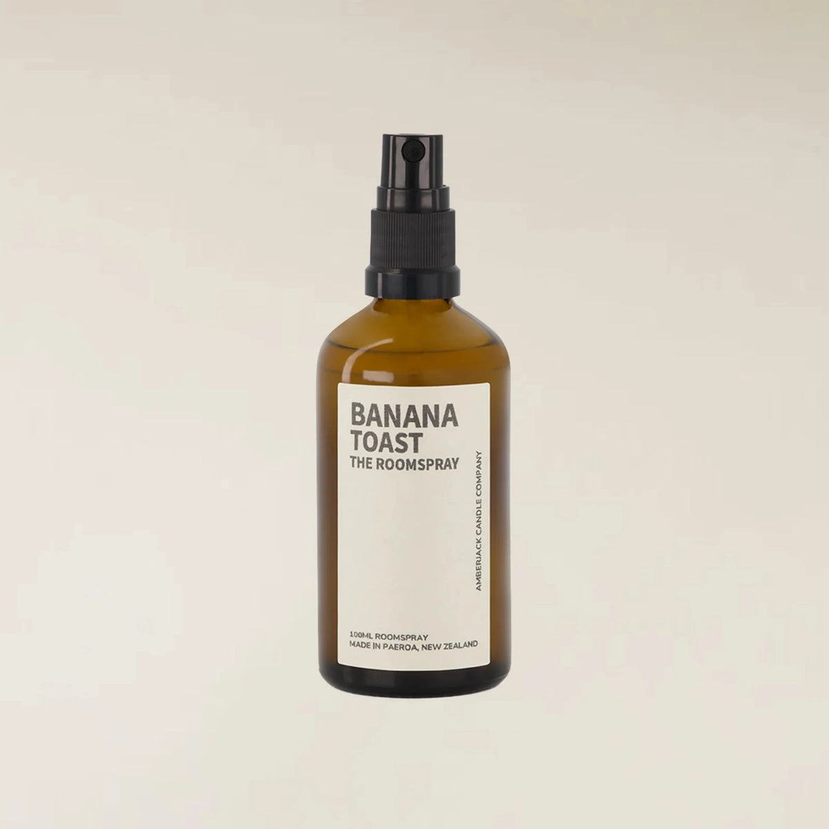An amber glass room spray bottle with a black spray nozzle and a cream-colored label that reads &