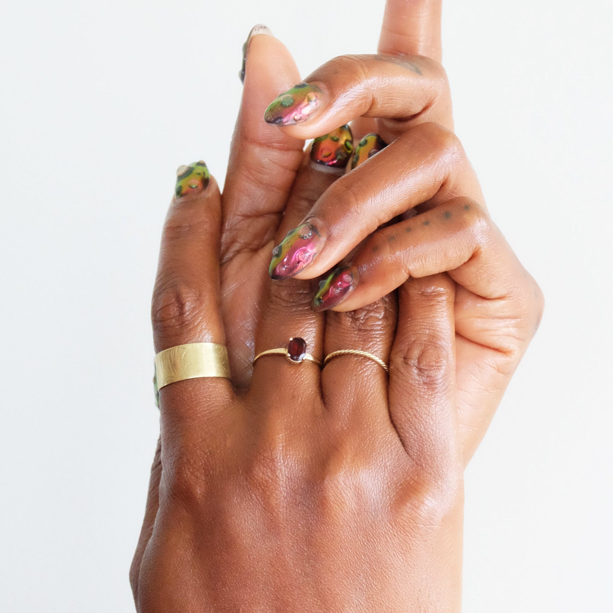 Hands with gold rings and colourful nail polish on a white background.
