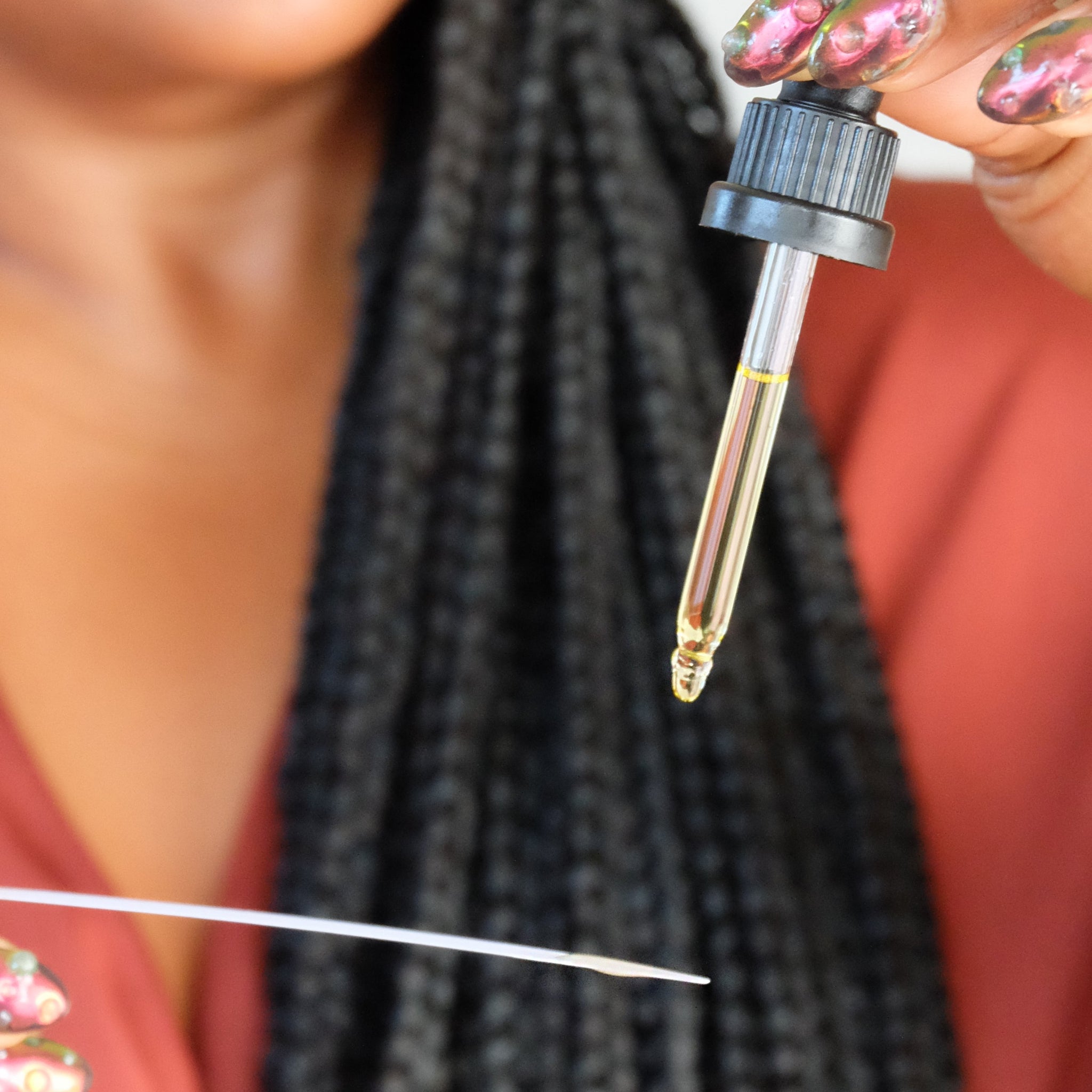 Close-up of a dropper with a liquid substance held by a person with braided hair.