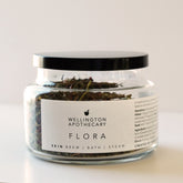 A glass apothecary jar containing the dried herbal tea blend of Flora Skin Brew.