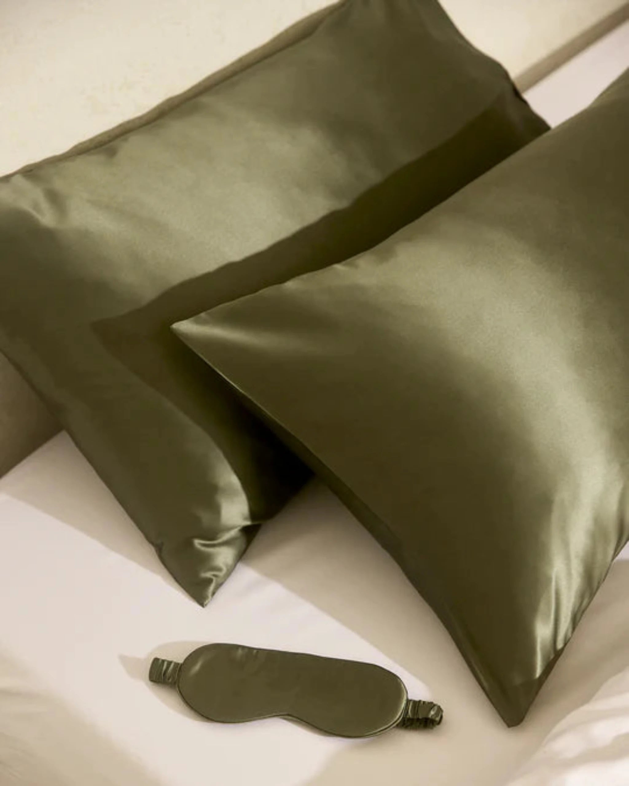 Two green silk pillows and a matching eye mask on a white surface.