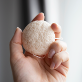 Hand holding a white konjac facial cleaning sponge.