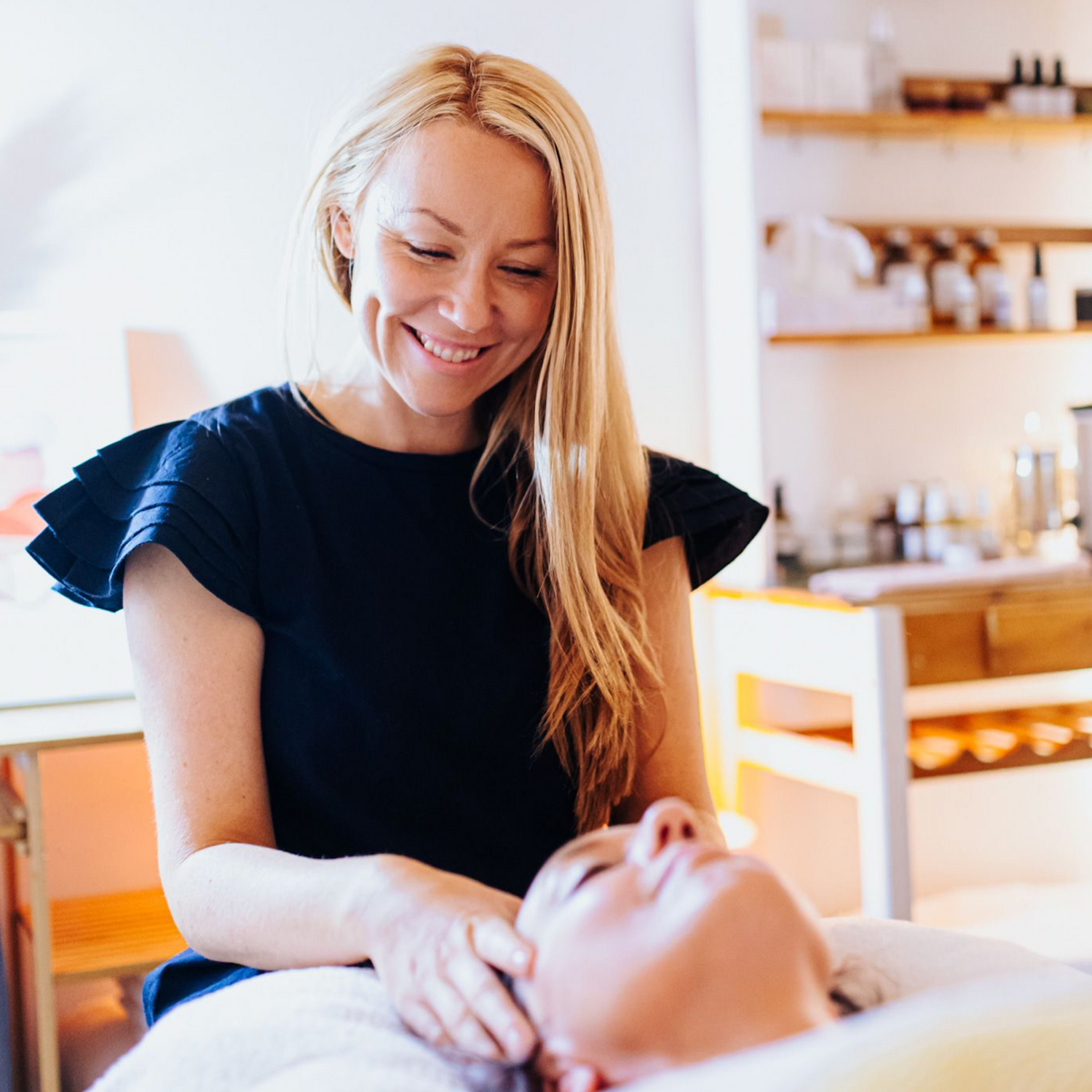 Holistic facialist smiling as she gives a facial massage in a brightly lite therapy room.