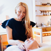 Holistic facialist smiling as she gives a facial massage in a brightly lite therapy room.