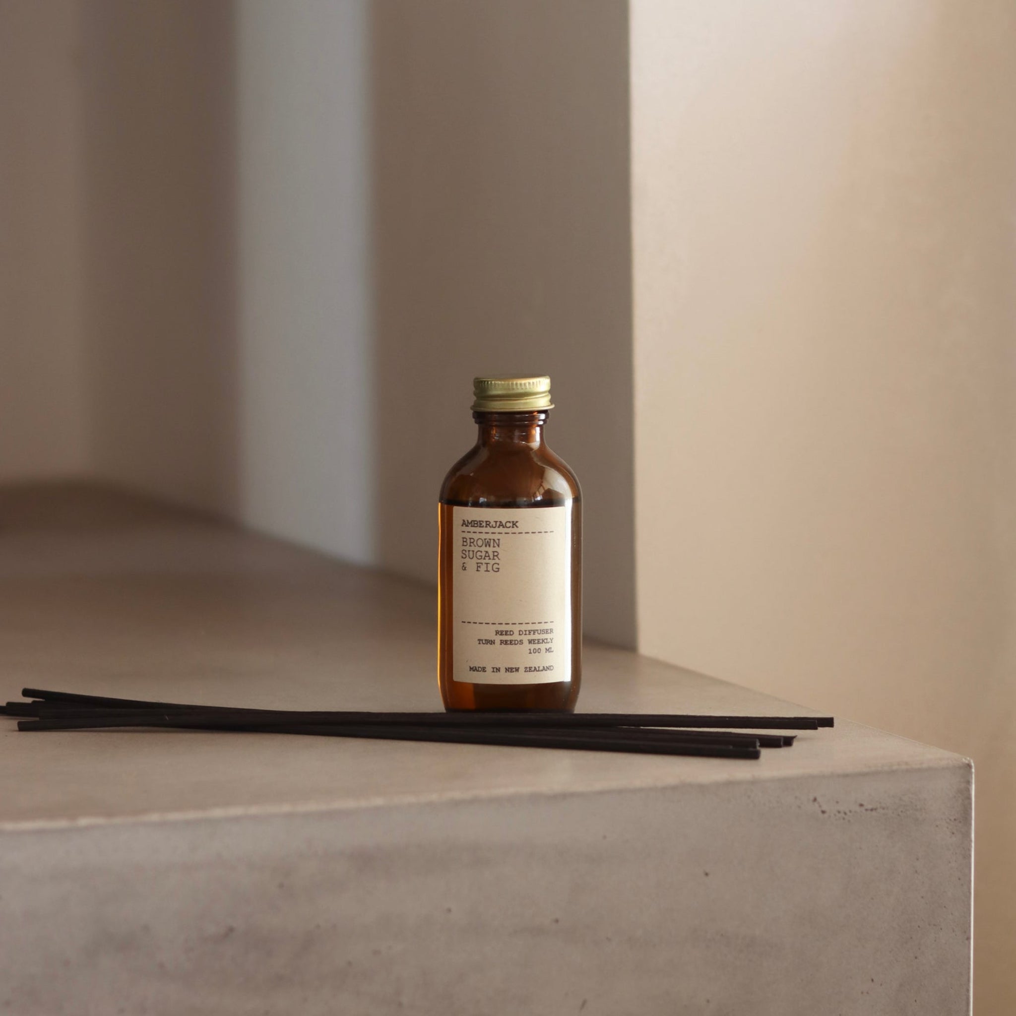 Amber glass bottle of brown sugar and fig reed diffuser on concrete block in warm light.