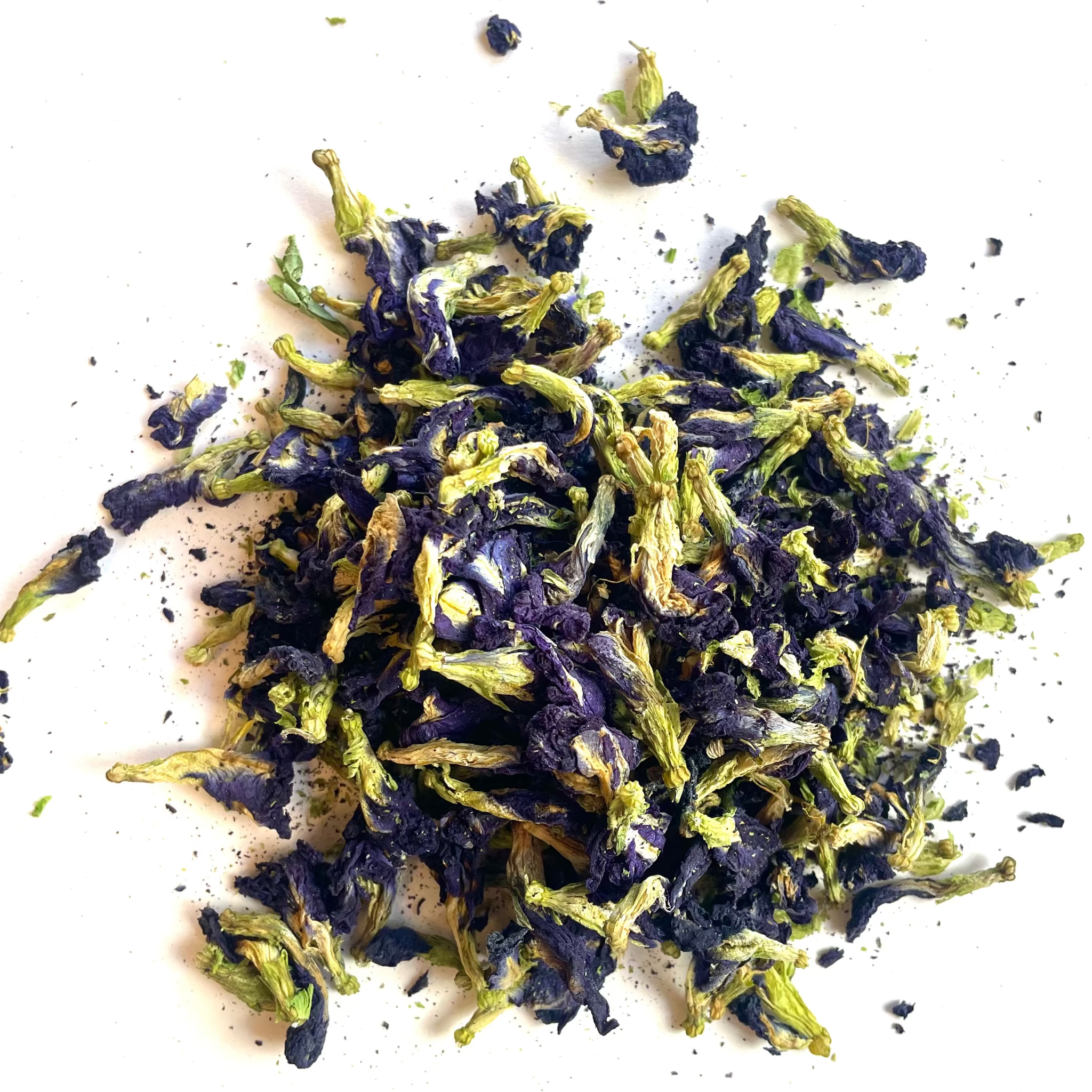 A small pile of dried butterfly pea flowers, showing deep purple-blue petals mixed with bright green stems, scattered on a plain white background.