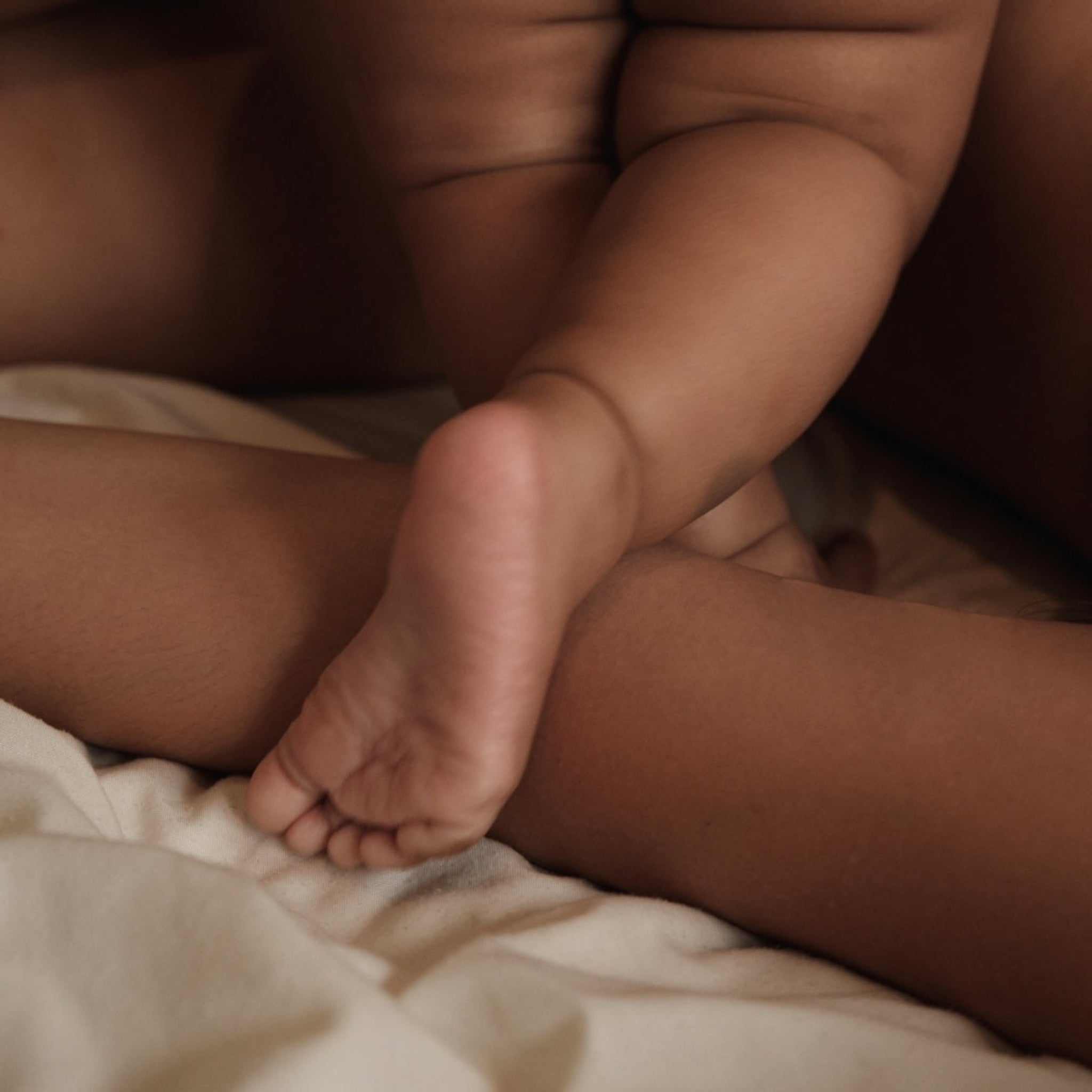 Chubby baby thighs and sole of foot resting against parents arm.