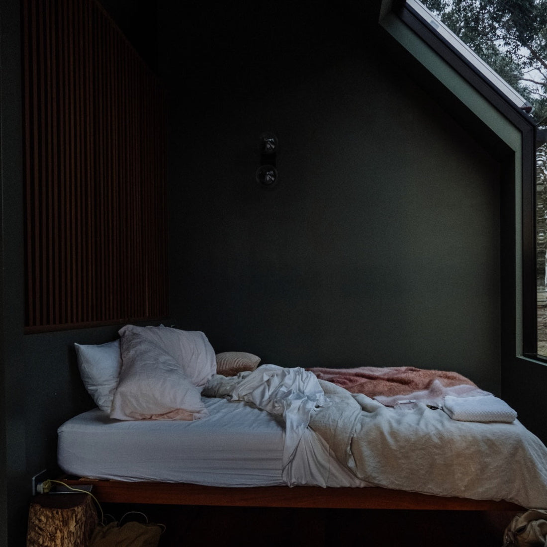 Cosy bedroom in dusk light, with dark green walls and soft, inviting bedding.
