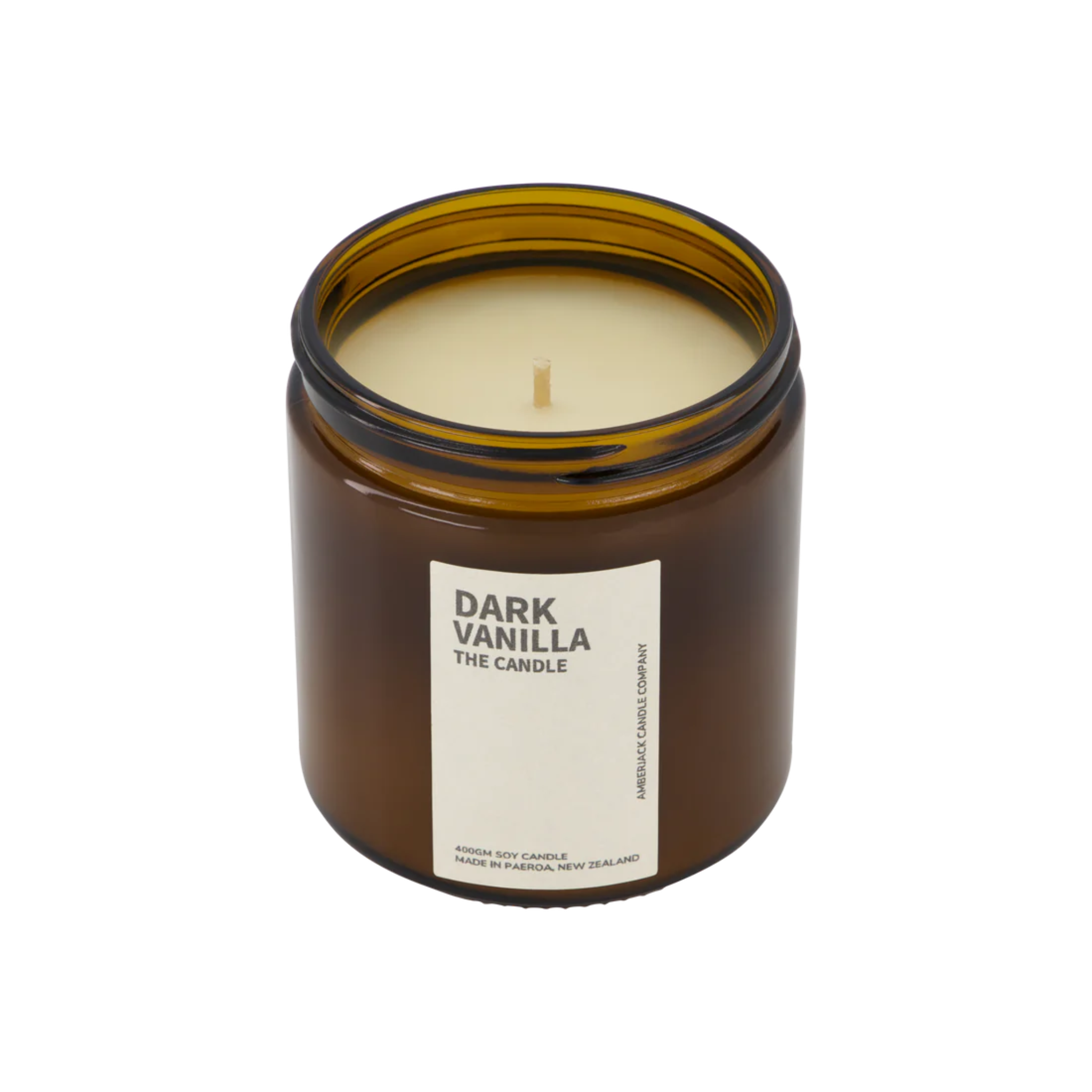 A large amber glass jar with brass lid containing dark vanilla candle on white background.
