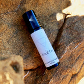 A small amber glass bottle of the Earth blend perfume oil displayed on a rock.