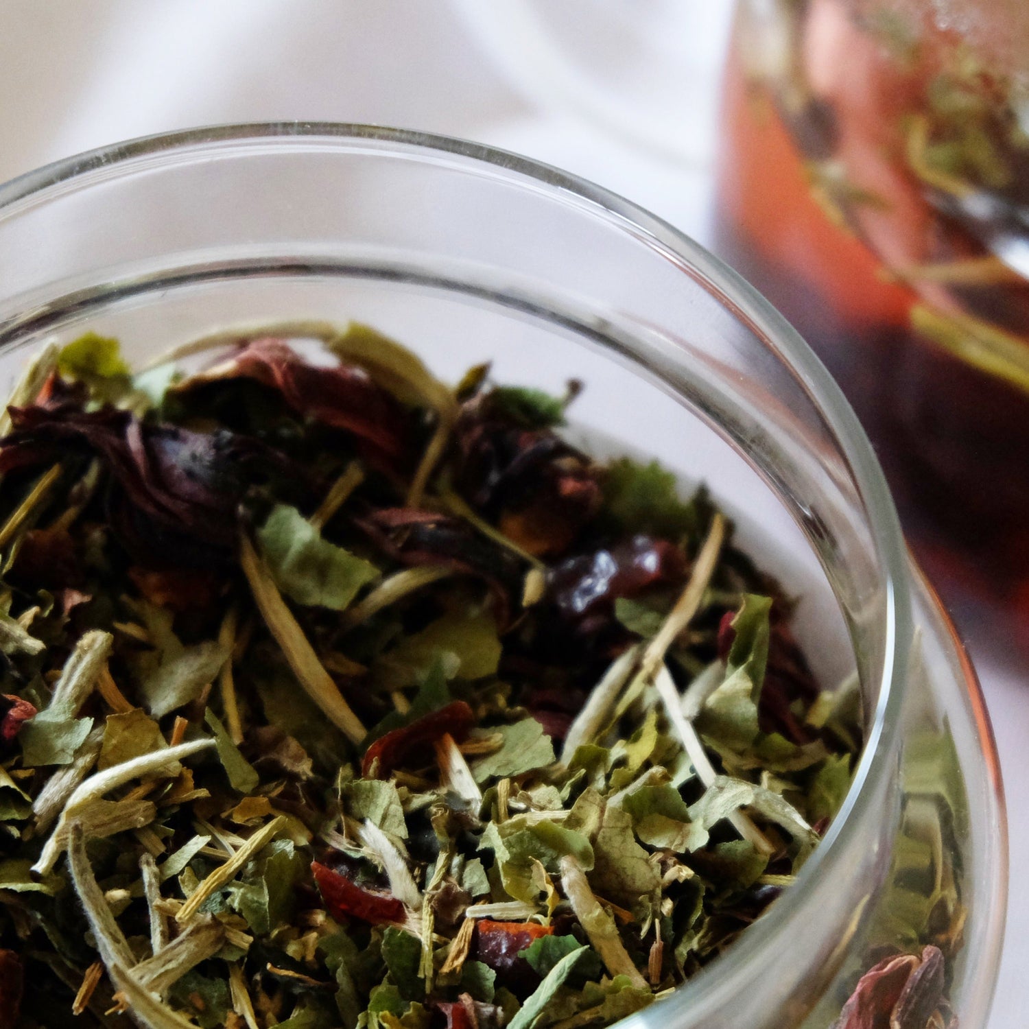 Close up of a glass apothecary jar containing the dried herbal tea blend of Flora Skin Brew.