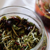 Close up of a glass apothecary jar containing the dried herbal tea blend of Flora Skin Brew.