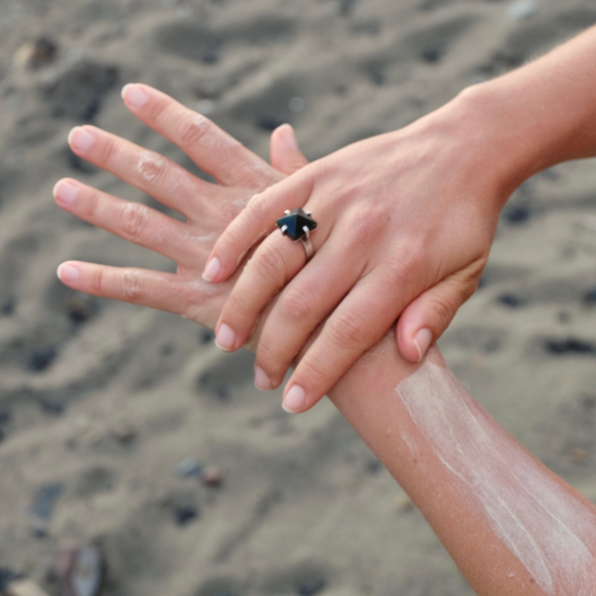 Applying hand cream on hands and arms with sandy beach background.