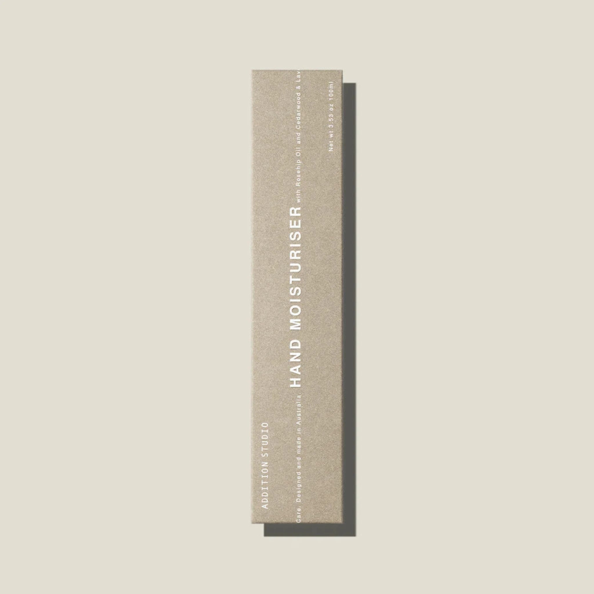An oat coloured box containing a tube of hand moisturiser on a beige surface.