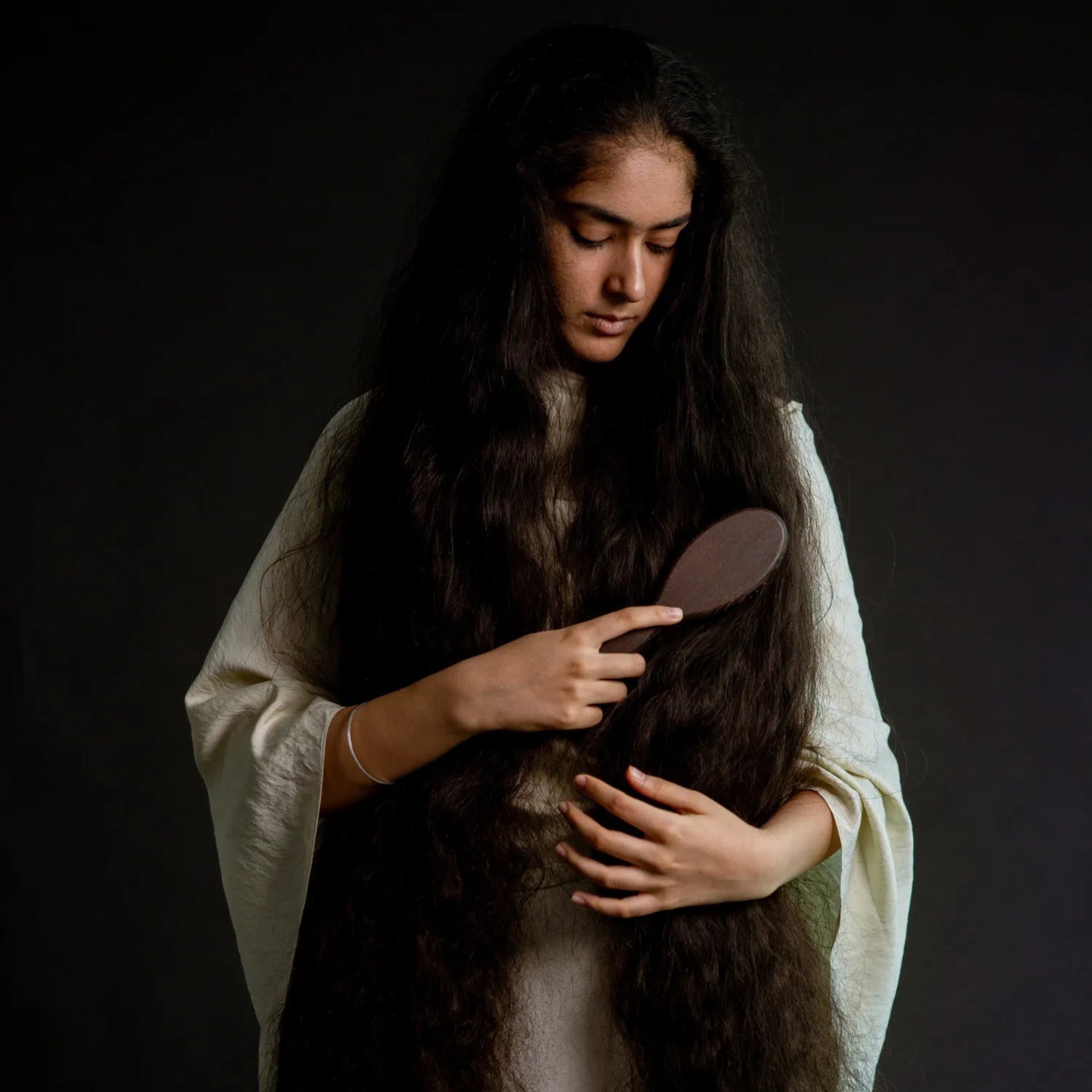 Woman with long hair holding a brush against a dark background