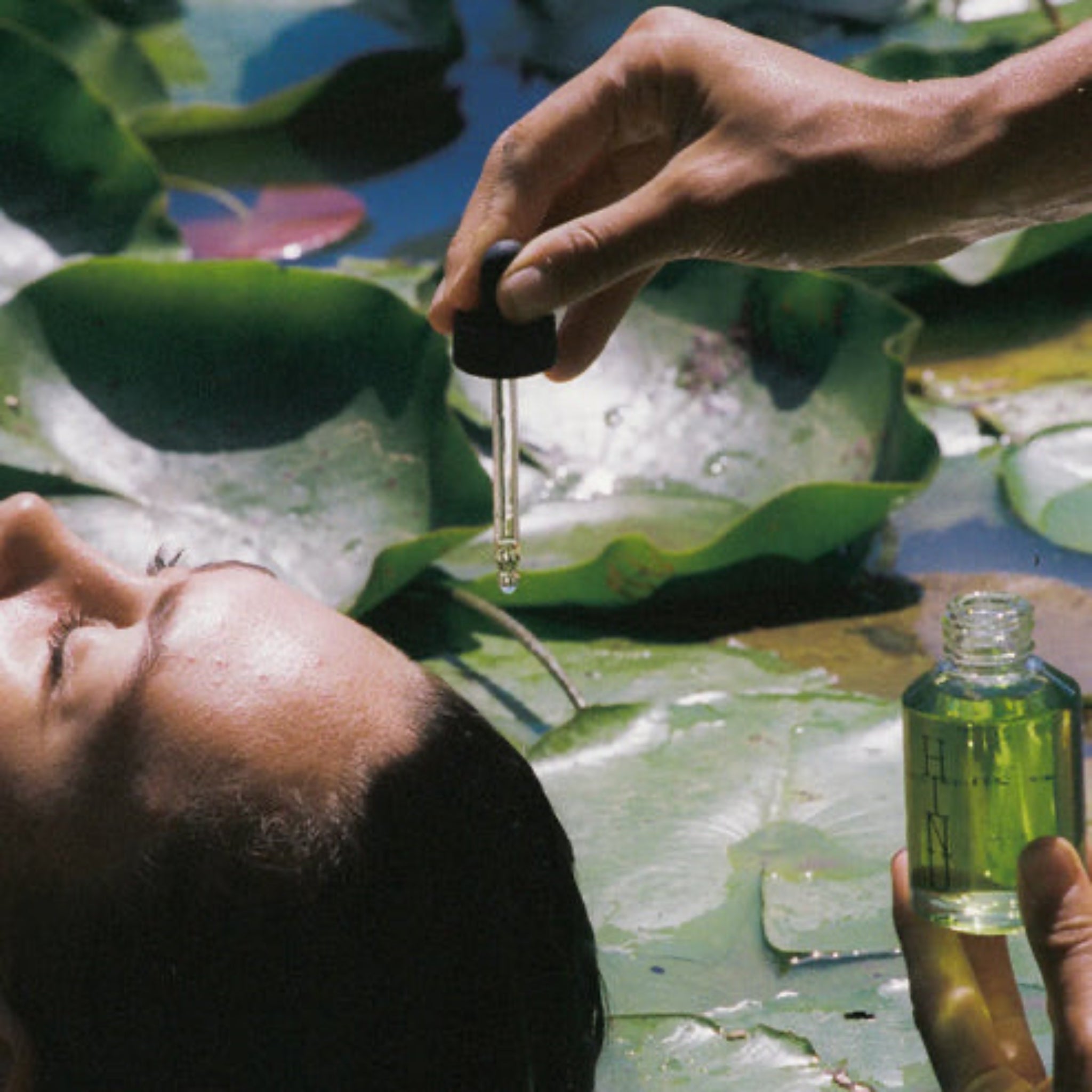 Person applying green oil from a dropper bottle on a leaf with a natural background