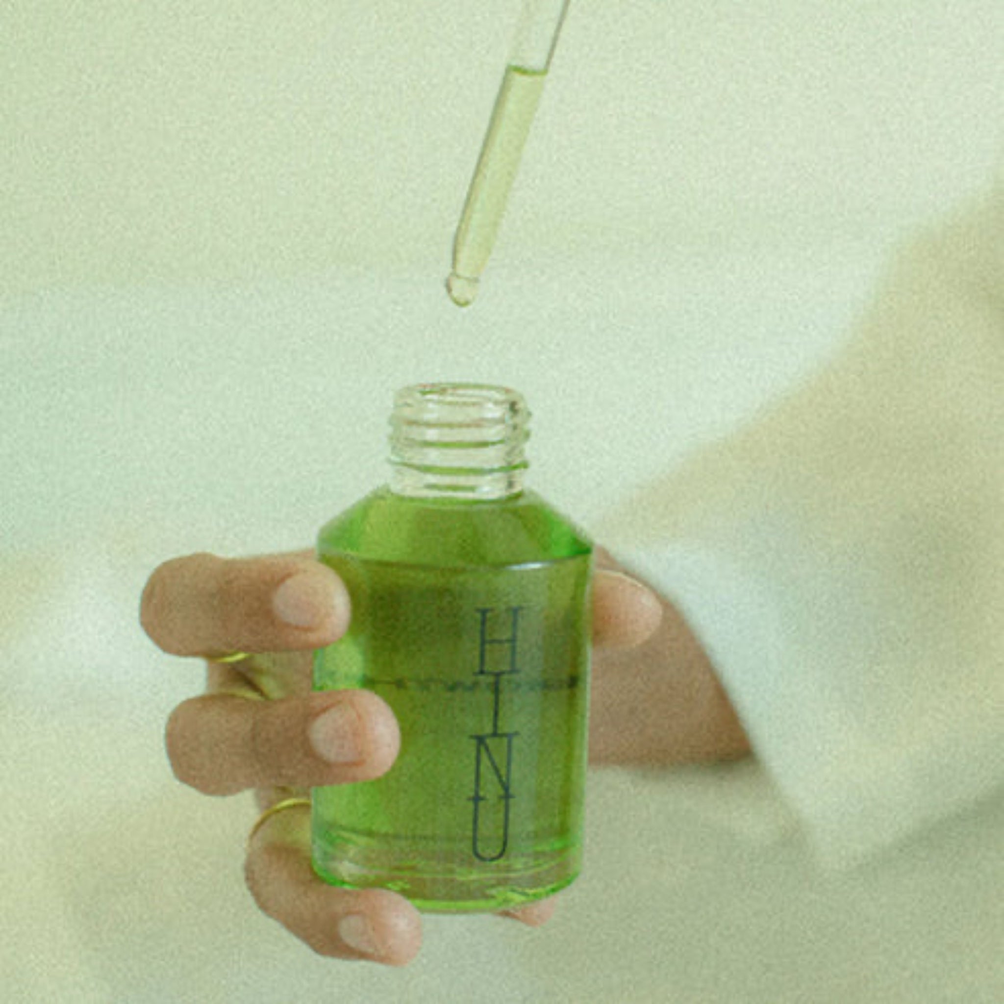Person holding a green bottle with a dropper, against a light background