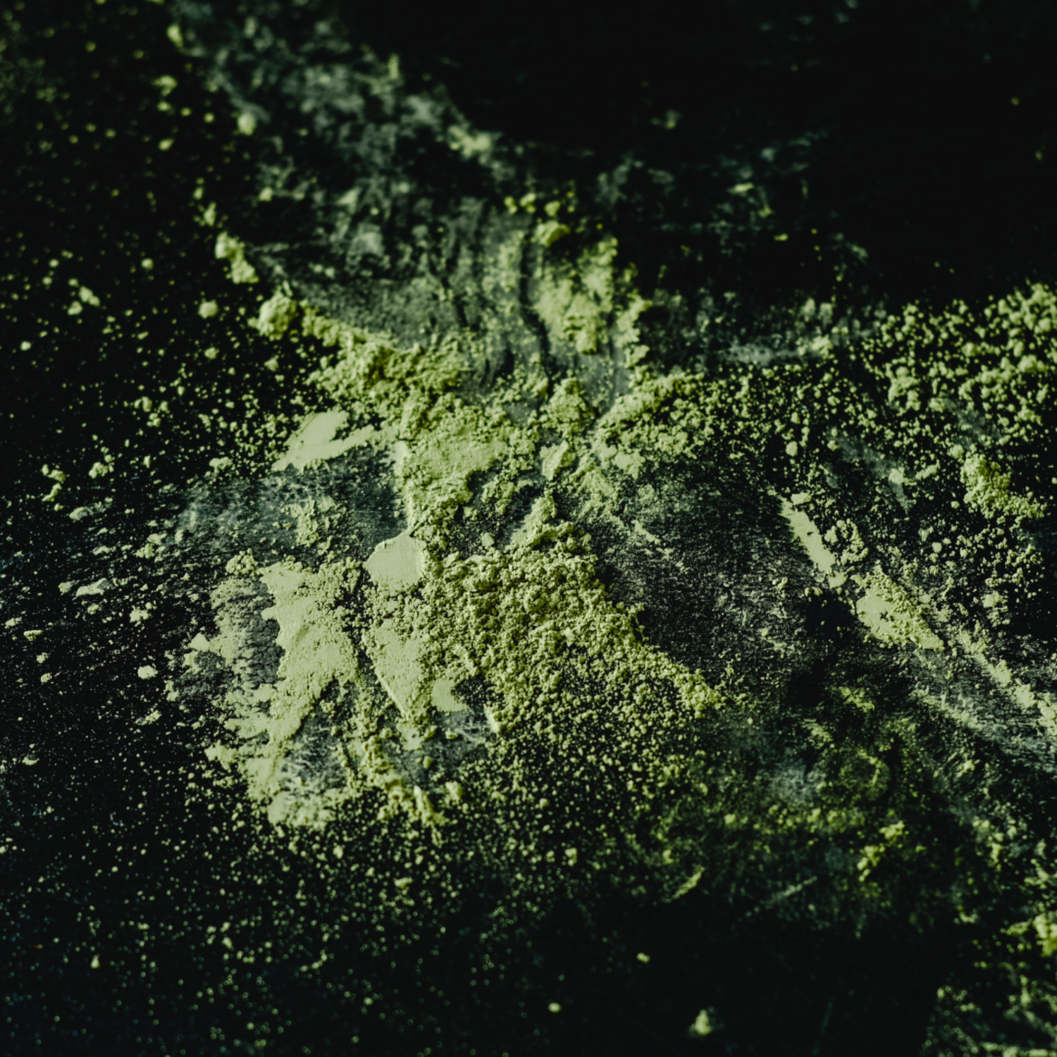 Bright green matcha powder scattered on a black surface.