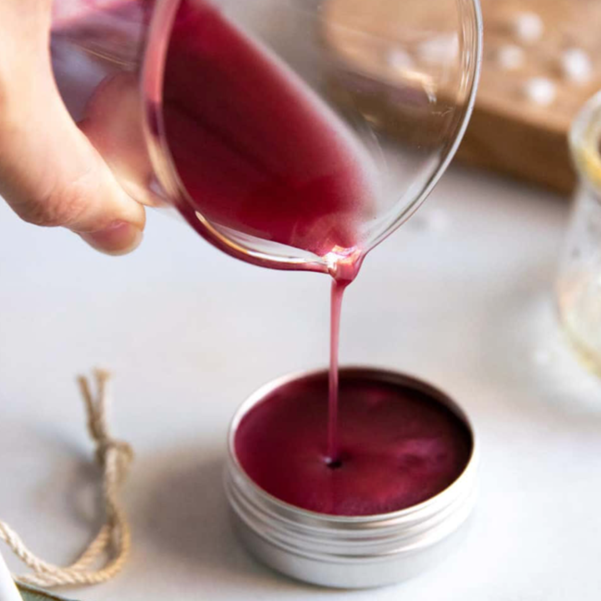 Liquid plum coloured lip tint being poured from a glass beaker into an aluminium tin.
