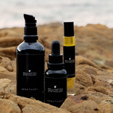 Three products in the Sanctuary collection, a body, a concentrated essential oil blend and a roll on perfume displayed on some coastal rocks.