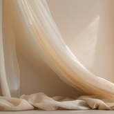 A creamy coloured silk curtain strewn across a creamy wall and over the floor in soft sunlight.