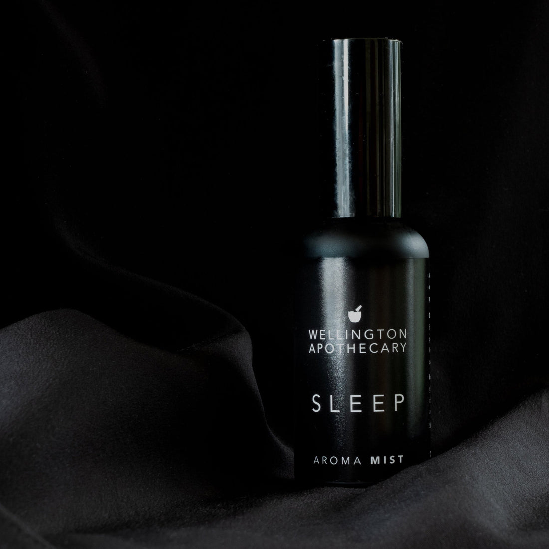 A black bottle of sleep aroma mist on black silk.