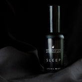 A black bottle of sleep aroma mist on black silk.