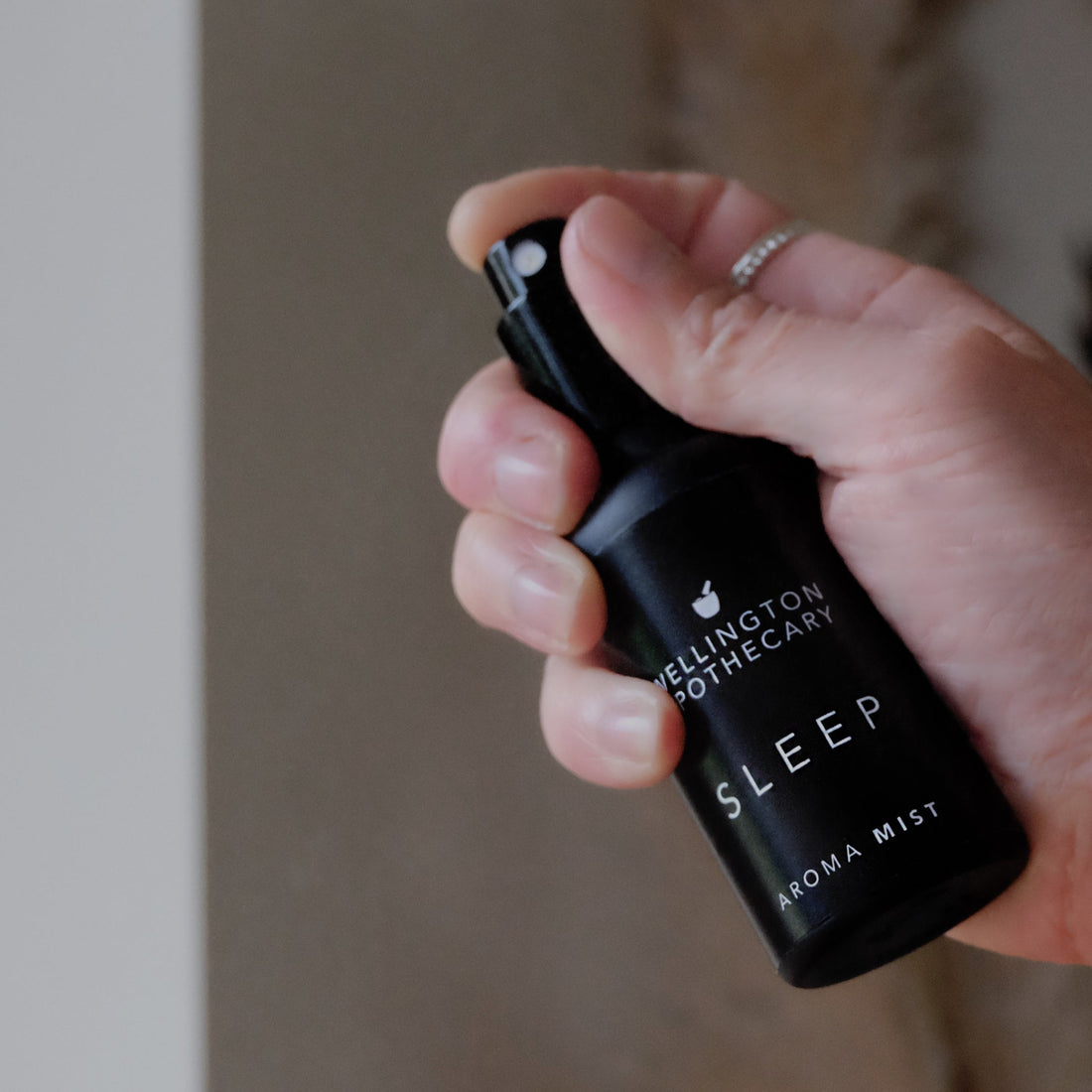A black bottle of sleep aroma mist held in hand being dispersed in a room.