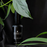 A black bottle of sleep aroma mist on black silk with surrounding greenery.