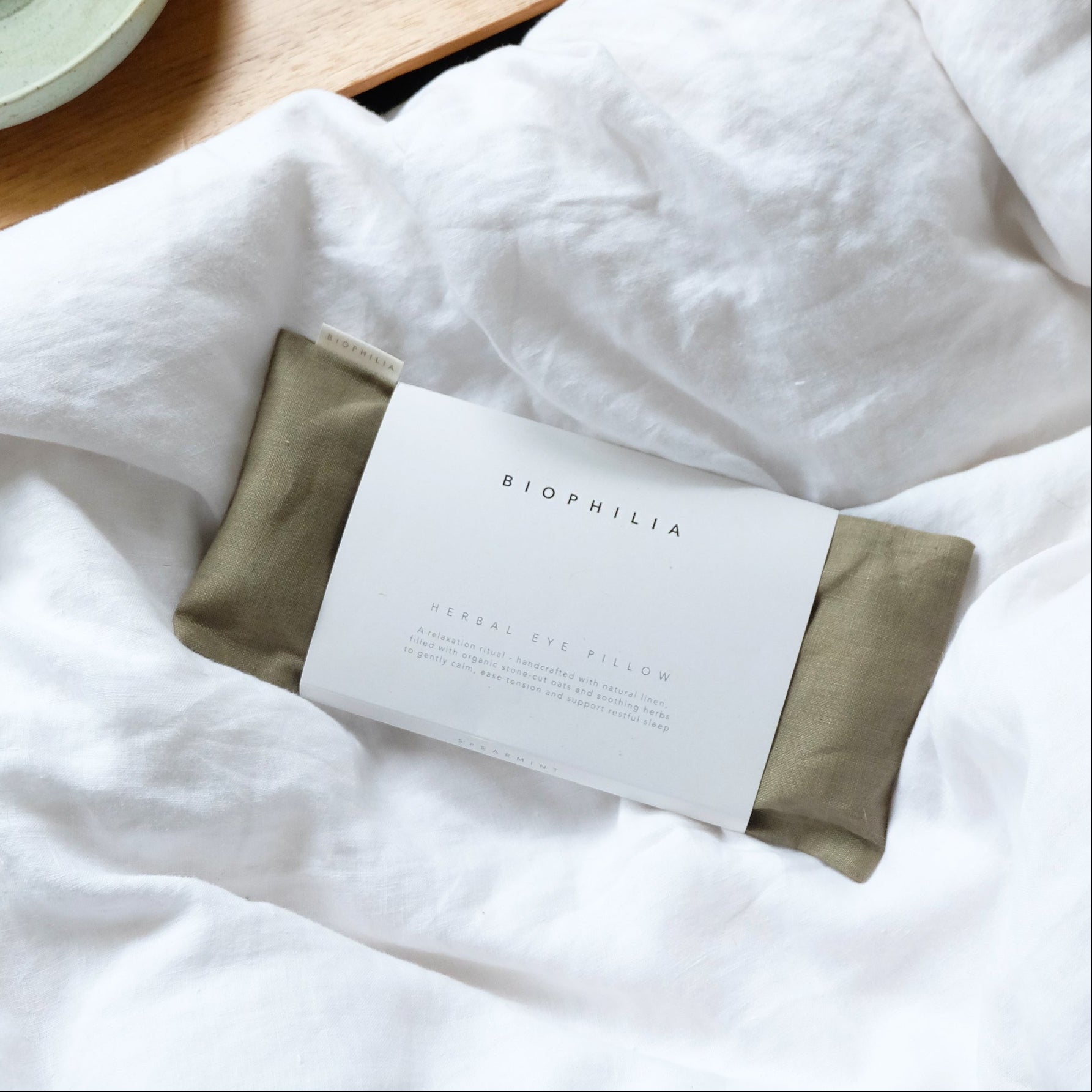 Green eye pillow on a white pillowcase and a ceramic incense burner on a wooden surface.