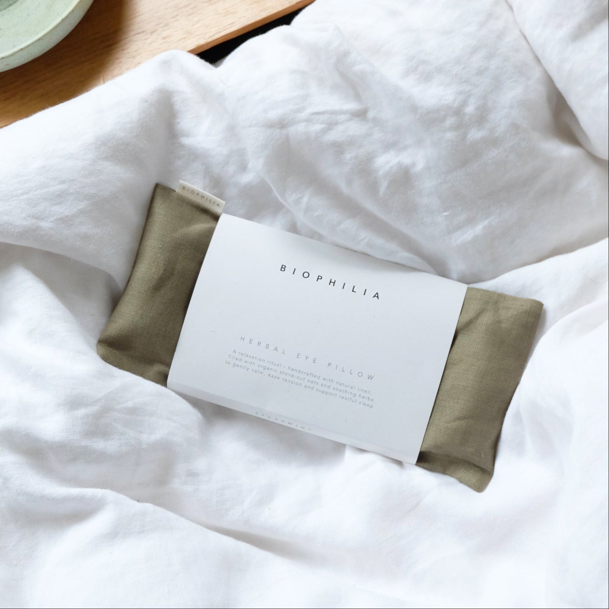 Green eye pillow on a white pillowcase and a ceramic incense burner on a wooden surface.