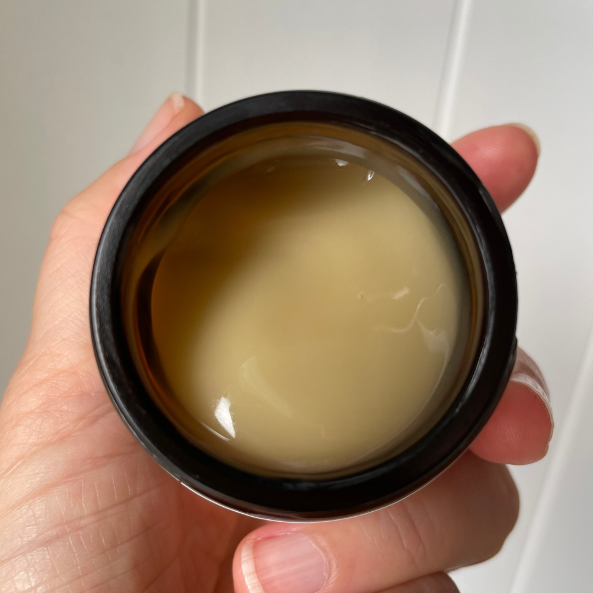 Hand holding an open jar of stellaria gel revealing its dewy texture and honey colour.
