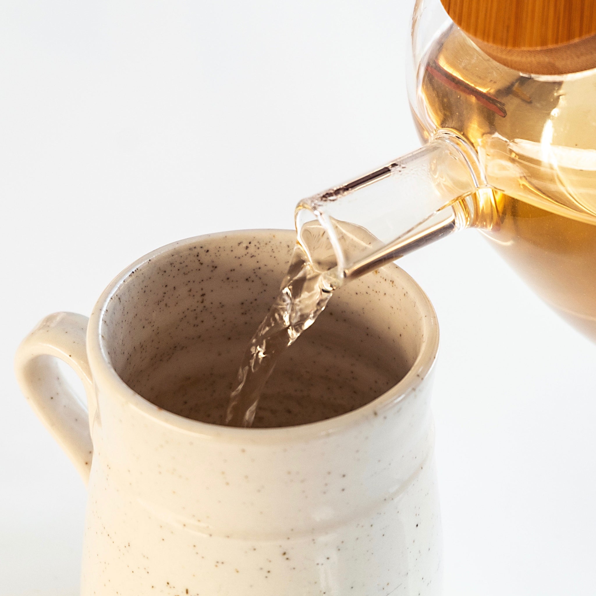 Herbal tea being poured from a glass teapot into a ceramic mug.