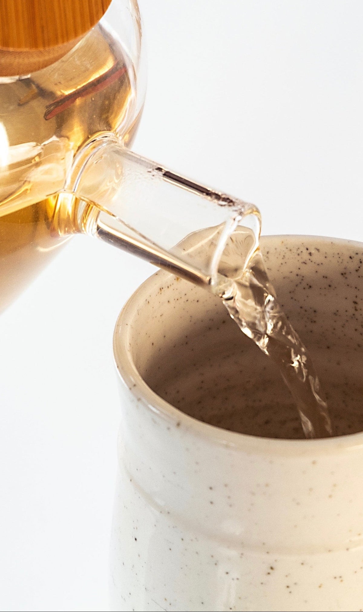 Herbal tea being poured from a glass teapot into a ceramic mug.