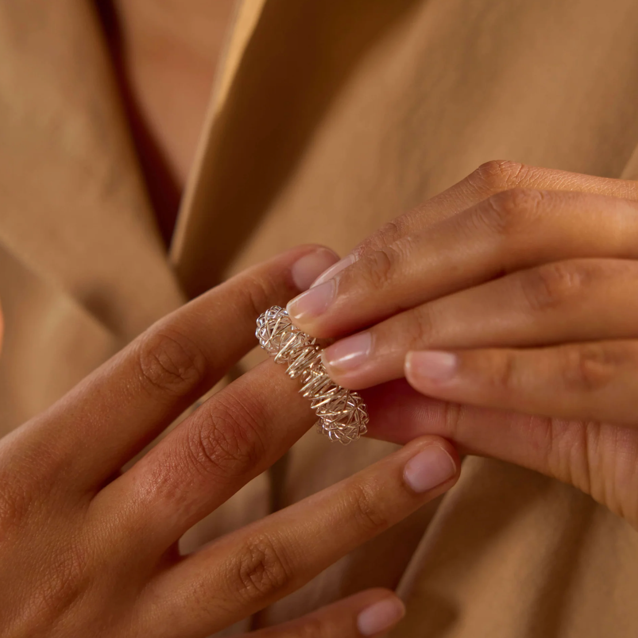 Close-up of a hand wearing a silver acupressure ring with a diamond on a beige background