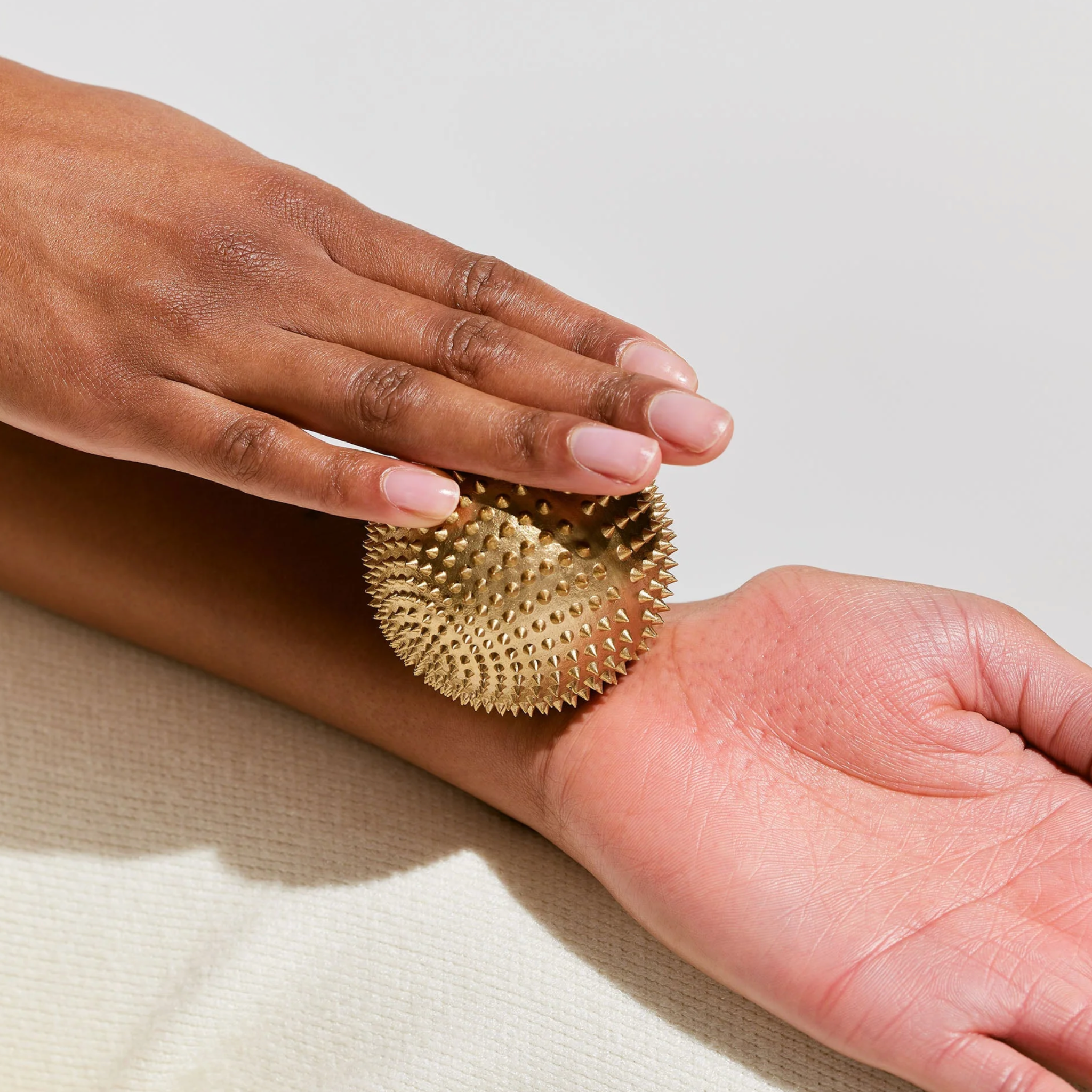 Hand holding a gold textured acupressure ball against a neutral background