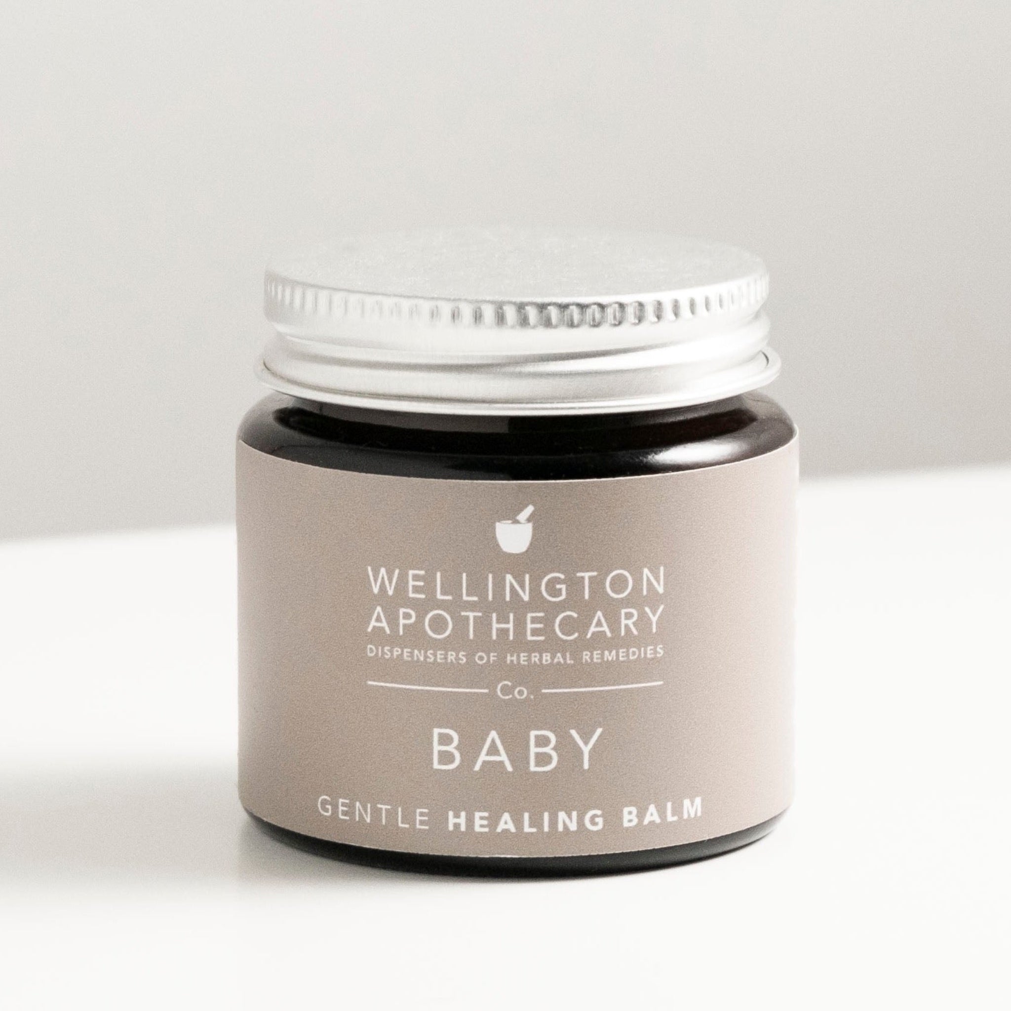 Amber glass jar of baby healing balm on white bench.