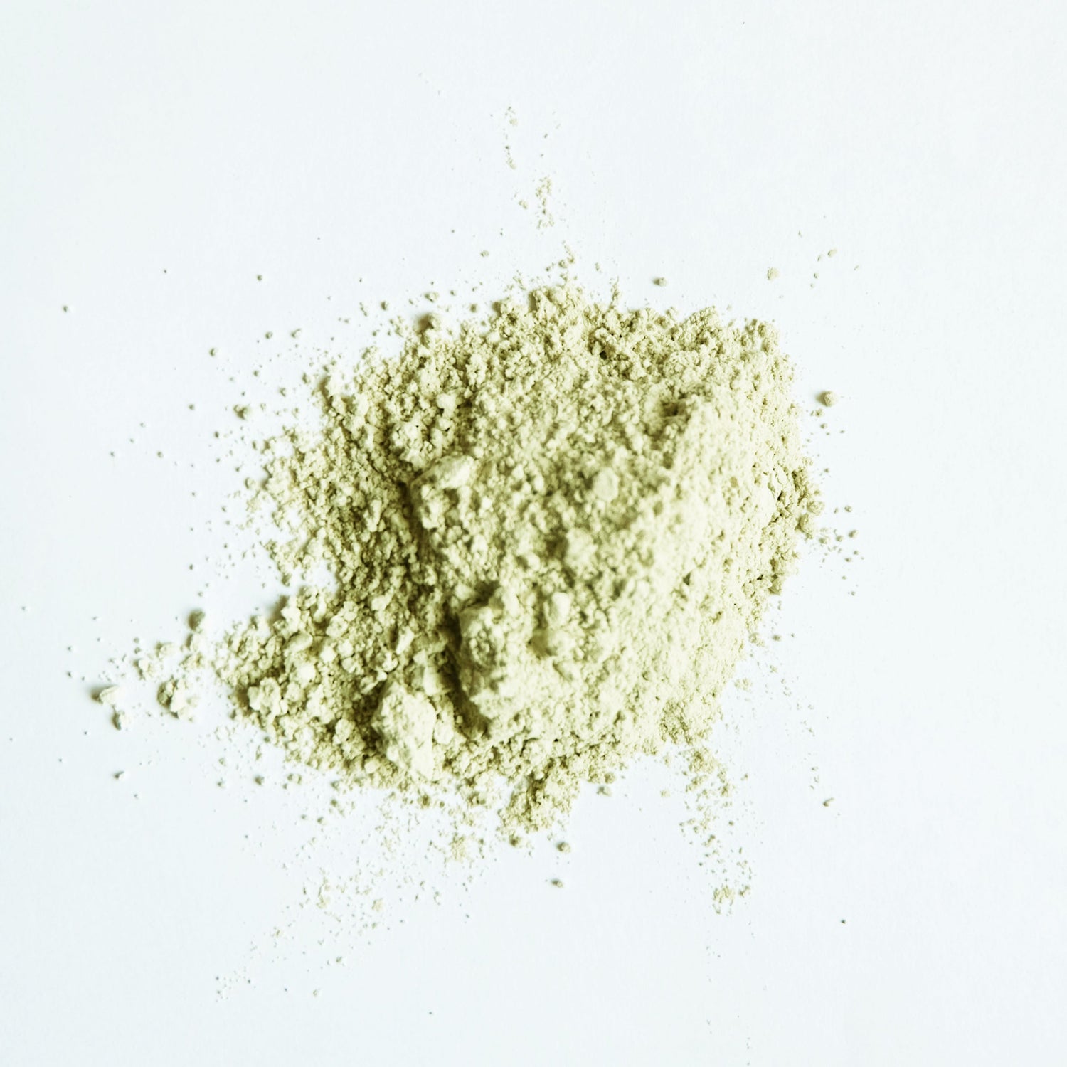 A small pile of green clay powder on white surface.
