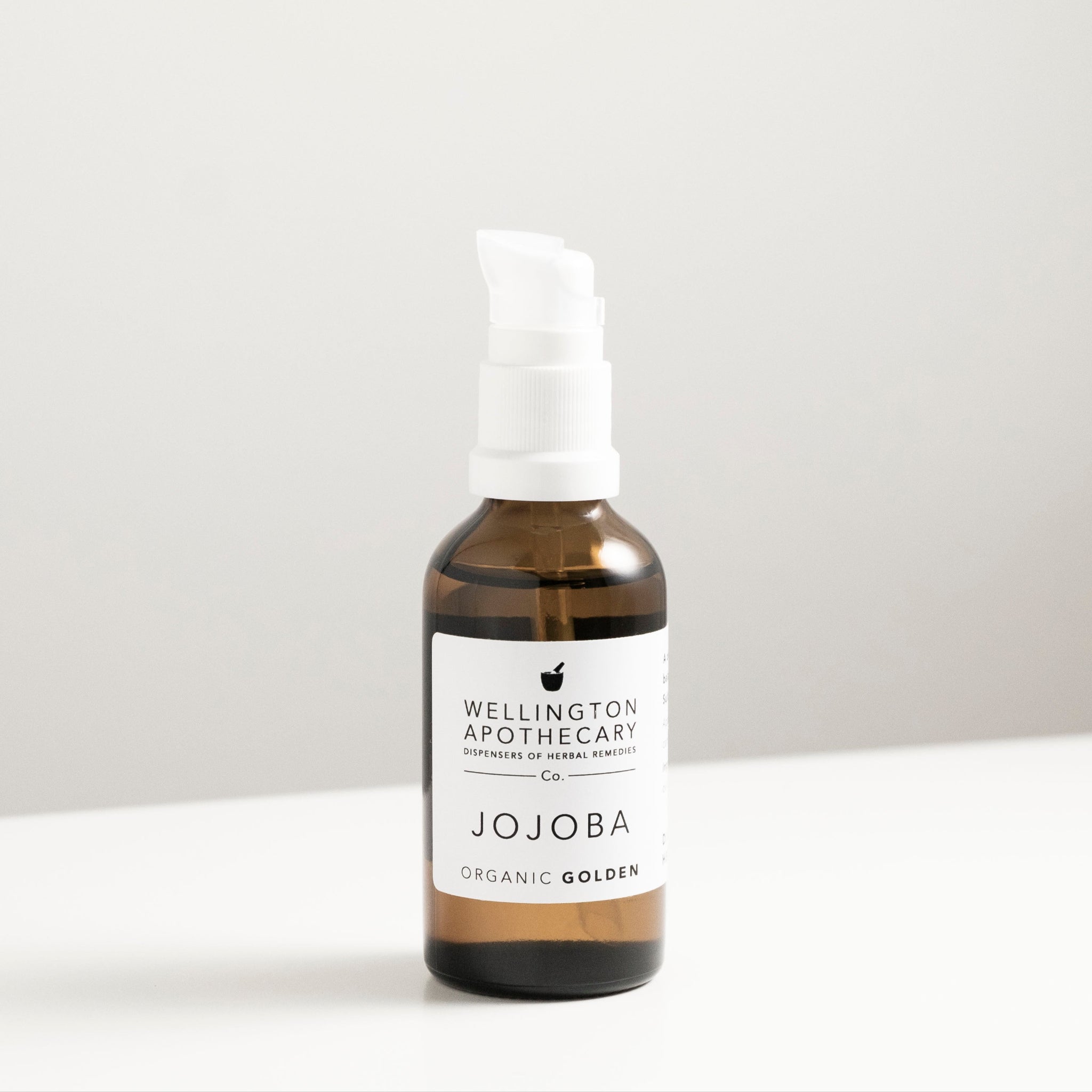 Amber glass bottle of jojoba oil on white bench.