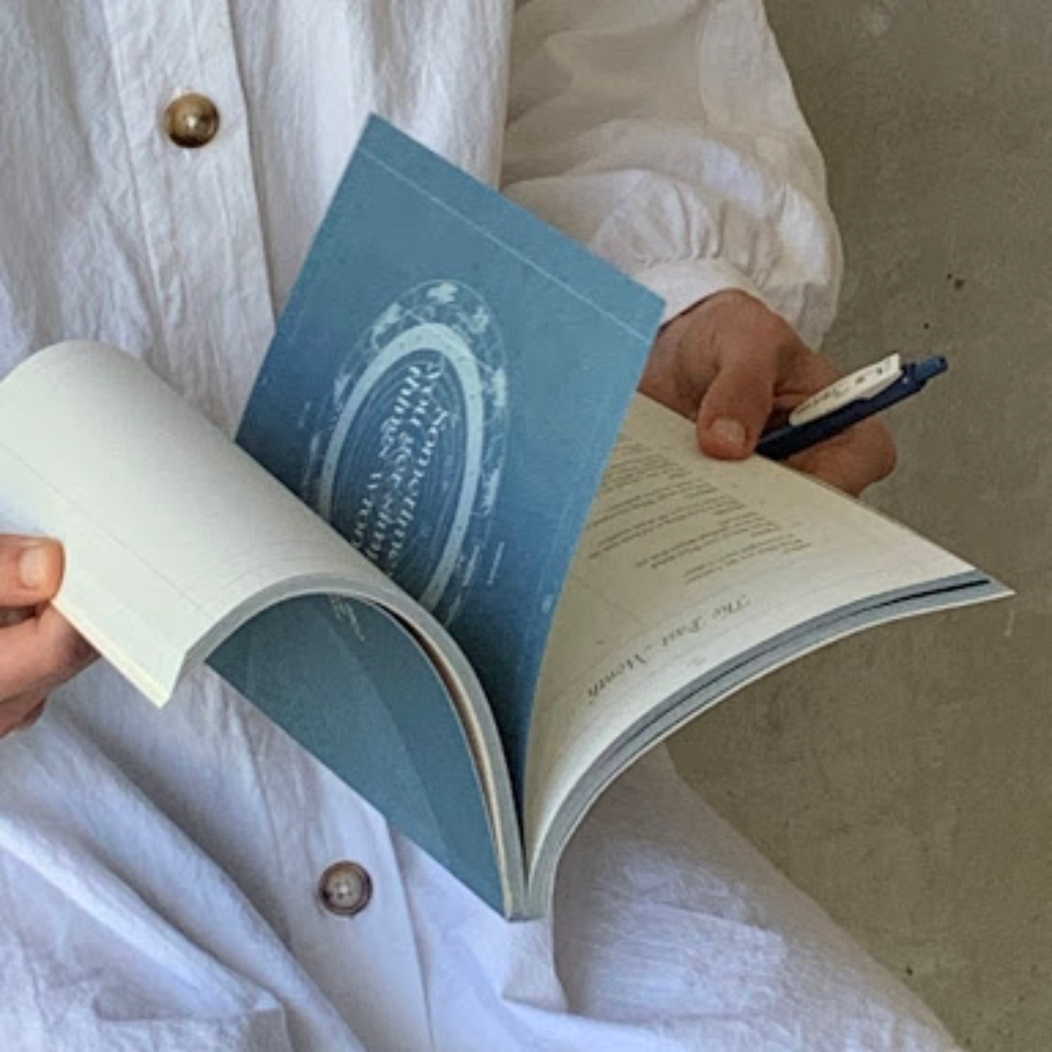 A woman in a white linen shirt flicks through the Moon Lists journal with a pen.