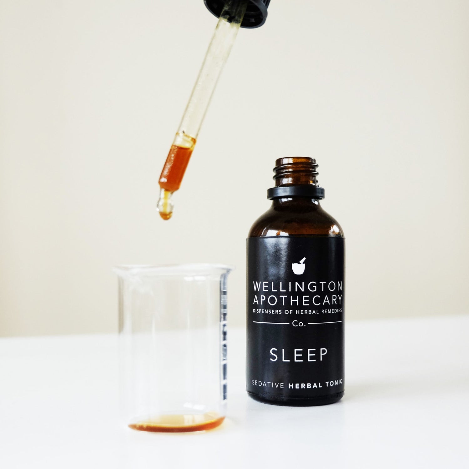 A bottle of sleep tonic with a dropper top dripping it into a glass beaker.