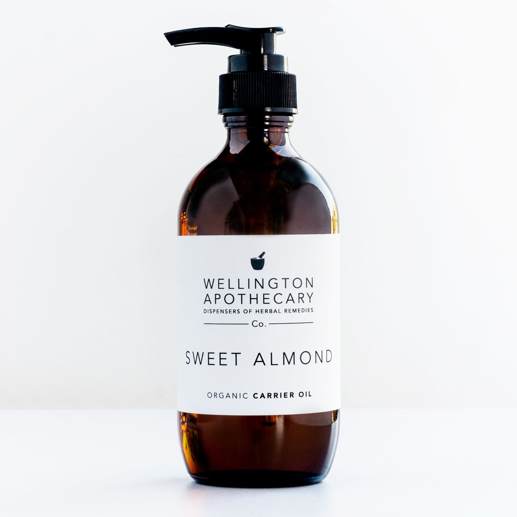 Large amber glass bottle of sweet almond oil on white bench.