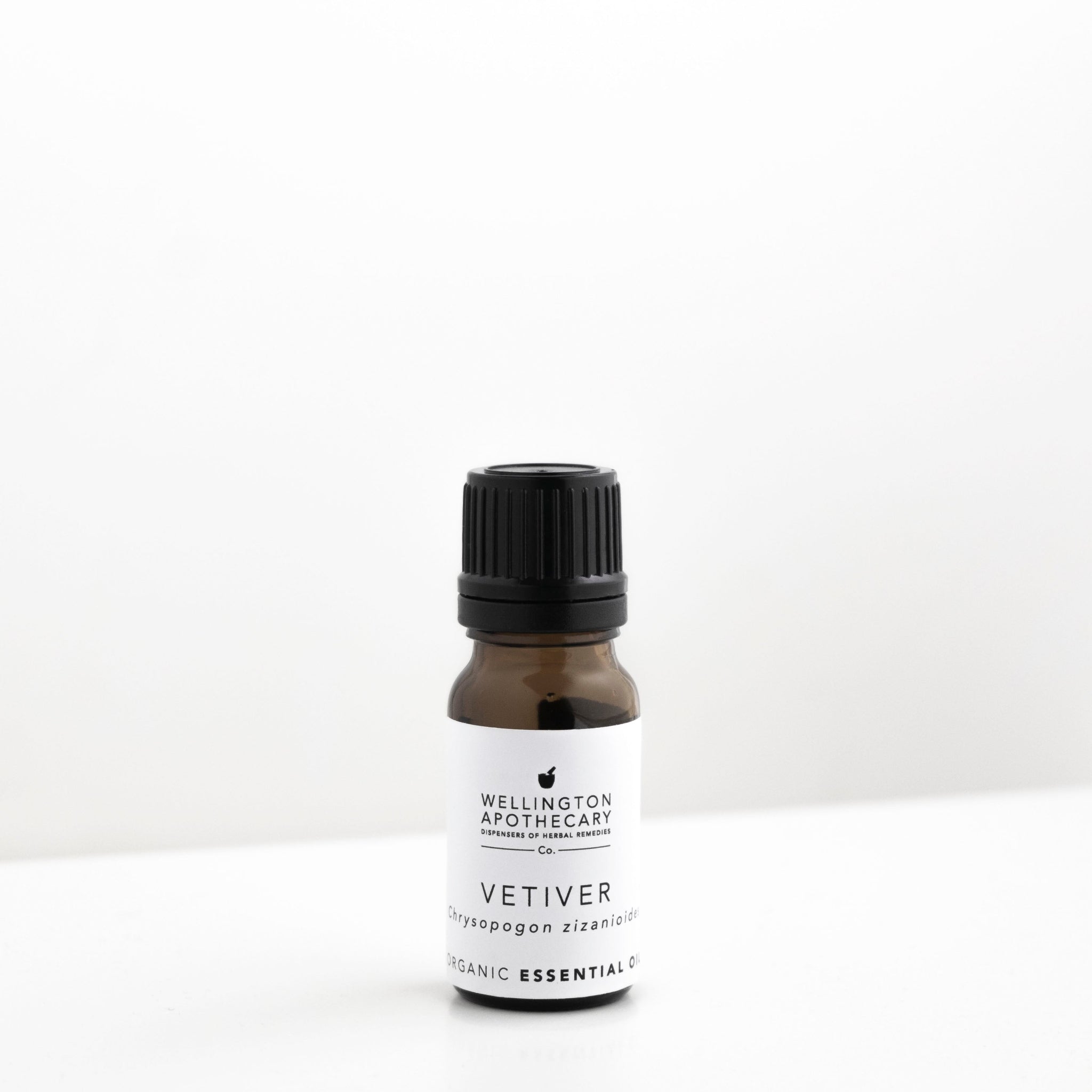 Small amber glass bottle of vetiver essential oil on white bench.