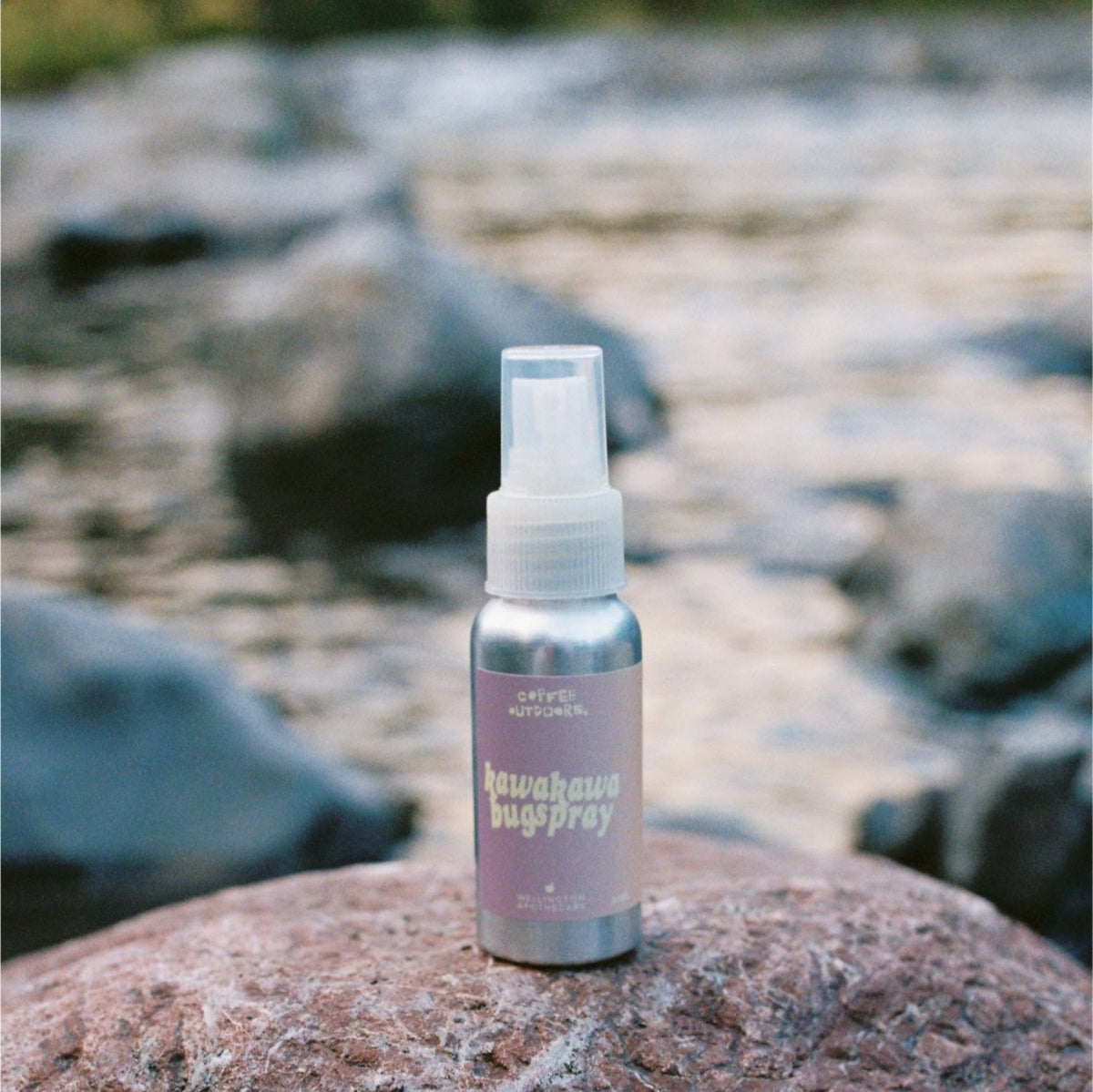 An aluminium bottle of Kawakawa Bug Spray on a rock by a river. 