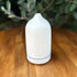 White essential oil diffuser on a wooden surface with greenery in the background