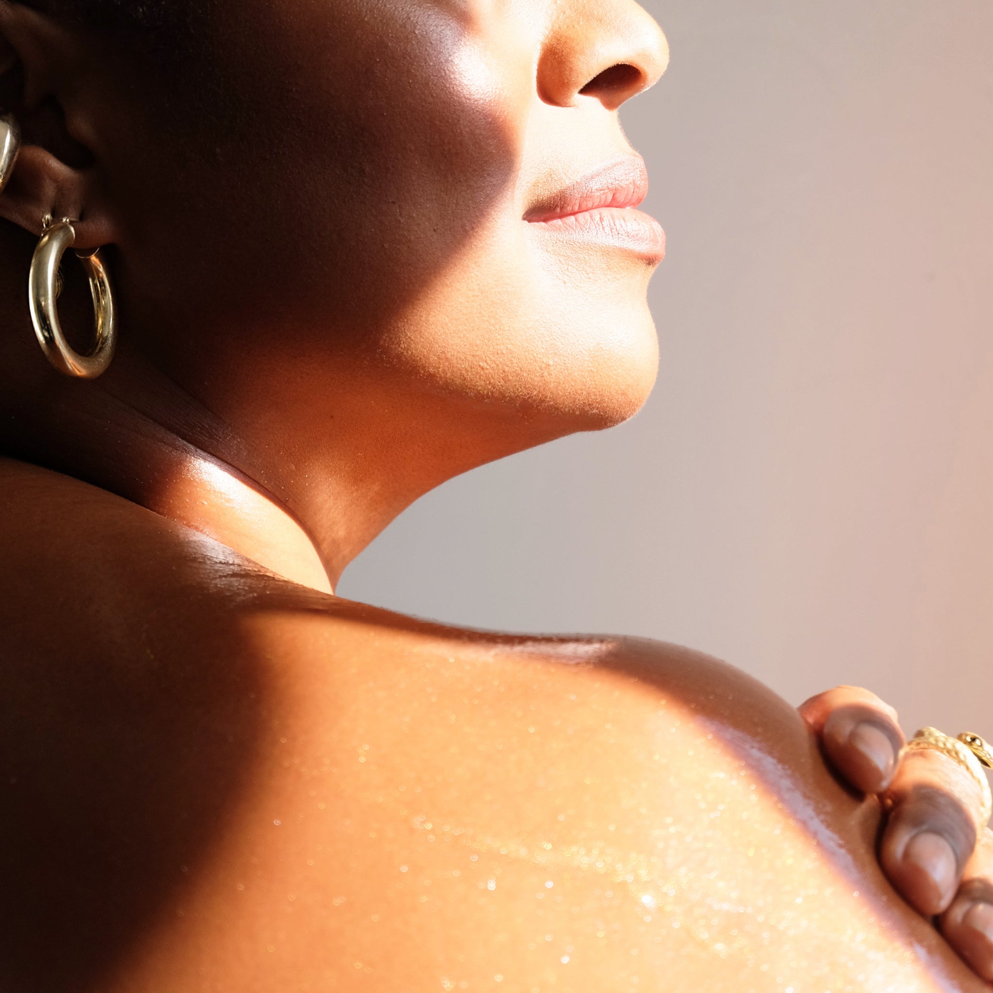 Woman with closed eyes, wearing gold hoop earrings, against a neutral background