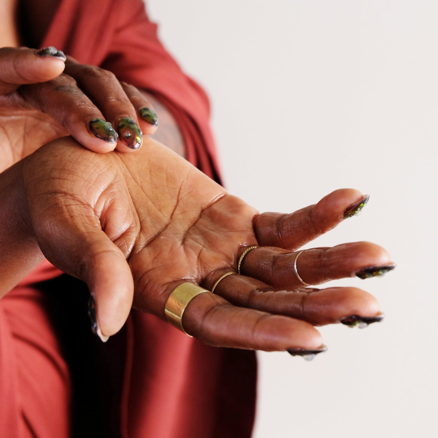 Close-up of two hands with gold rings on a plain background