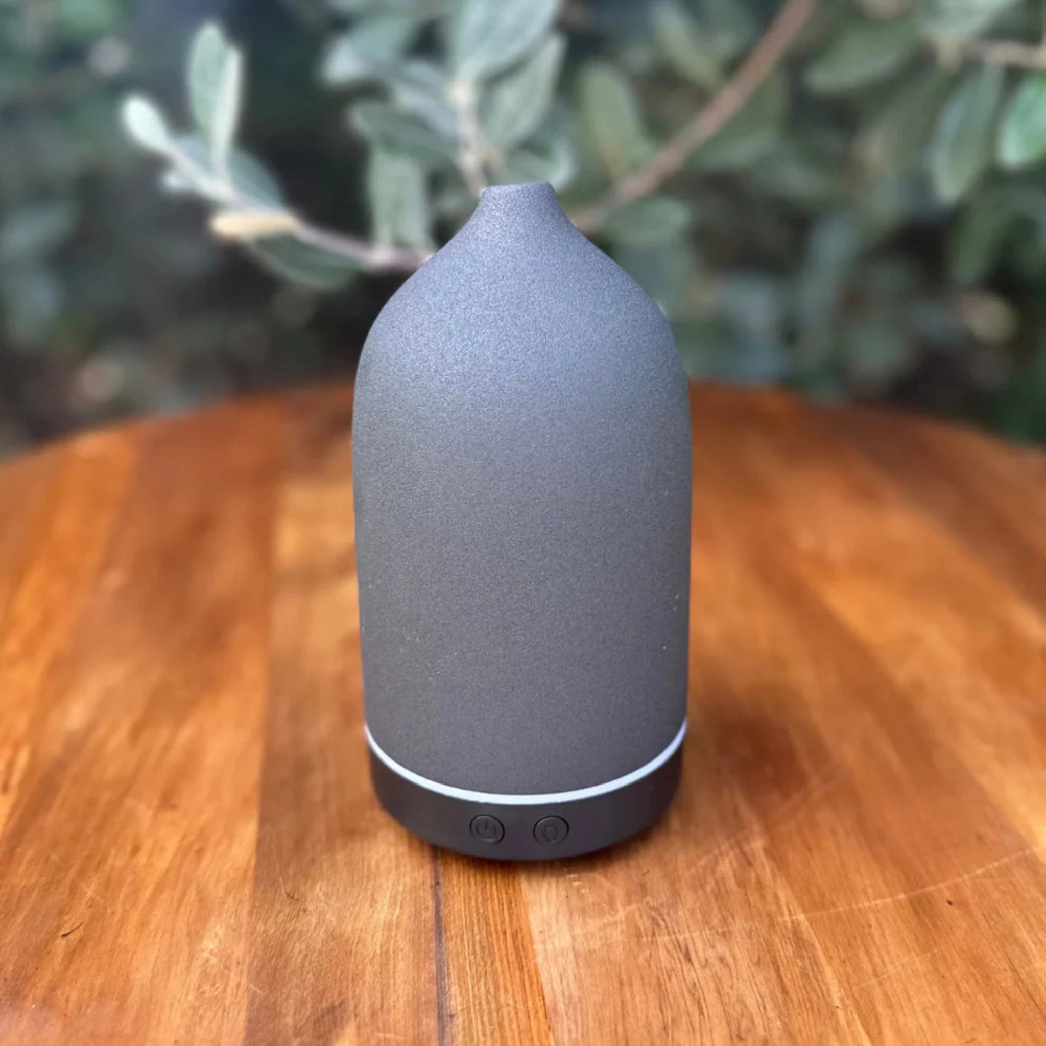 Gray diffuser on a wooden surface with a blurred green plant background