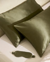 Two green silk pillows and a matching eye mask on a white surface.