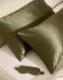Two green silk pillows and a matching eye mask on a white surface.
